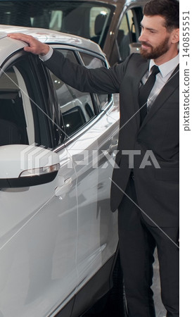 Vertical Video Stylish man is choosing new automobile walking around luxury car and touching it in car dealership. Rich people, transportation and business class vehicles concept. Vertical Video Stylish man is choosing new automobile walking around luxury car and touching it in car dealership. Rich people, transportation and business class vehicles concept. 140855551