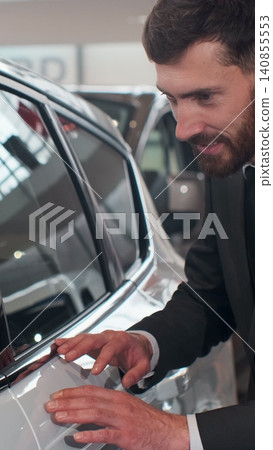 Vertical Video Stylish man is choosing new automobile walking around luxury car and touching it in car dealership. Rich people, transportation and business class vehicles concept. Vertical Video Stylish man is choosing new automobile walking around luxury car and touching it in car dealership. Rich people, transportation and business class vehicles concept. 140855553