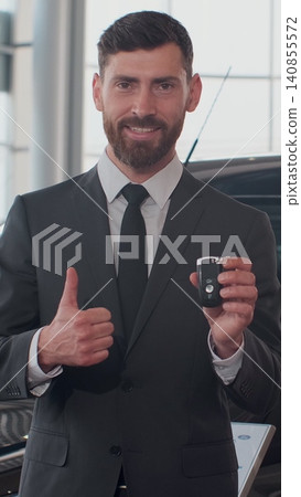 Vertical Video Professional car salesman smiling happily holding car keys standing in front of new cars at the dealership. Vertical Video Professional car salesman smiling happily holding car keys standing in front of new cars at the dealership. 140855572