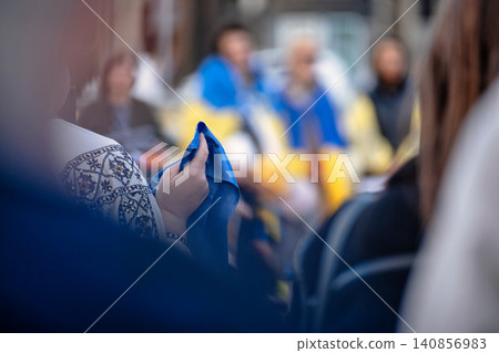 A close-up of a person holding a blue cloth, with a blurred background of people, some dressed in blue and yellow, suggesting participation in a gathering or event A close-up of a person holding a blue cloth, with a blurred background of people, some dressed in blue and yellow, suggesting participation in a gathering or event 140856983