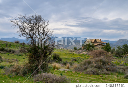 Expansive landscape with a rustic house nestled against a mountainous backdrop Expansive landscape with a rustic house nestled against a mountainous backdrop 140857561
