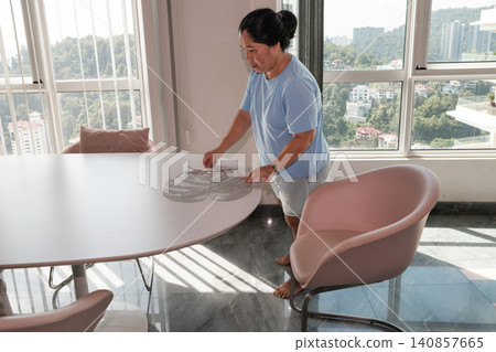 Woman prepares dining table in a city apartment with a view of hills and buildings during daytime Woman prepares dining table in a city apartment with a view of hills and buildings during daytime 140857665