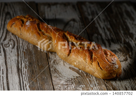 Freshly baked rustic bread loaf resting on an aged wooden table illuminated Freshly baked rustic bread loaf resting on an aged wooden table illuminated 140857702