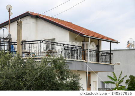 Cozy hillside residence with a red-tiled roof and balcony in a serene neighborhood during cloudy afternoon Cozy hillside residence with a red-tiled roof and balcony in a serene neighborhood during cloudy afternoon 140857956
