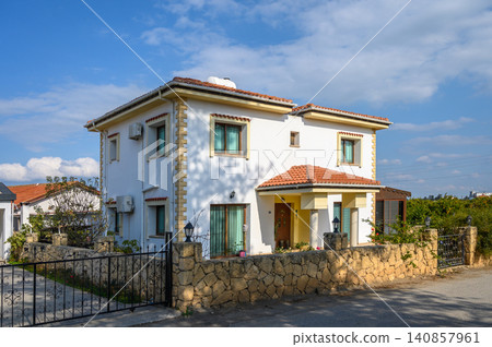 Charming white house with lush garden under blue sky in a peaceful neighborhood Charming white house with lush garden under blue sky in a peaceful neighborhood 140857961