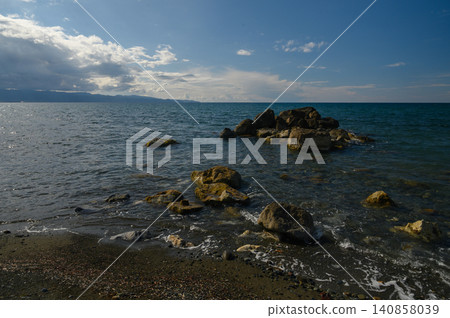 Vibrant coastal tranquility where waves gently caress the rugged rocks under a vast blue sky midday Vibrant coastal tranquility where waves gently caress the rugged rocks under a vast blue sky midday 140858039