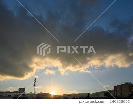 Dramatic sunset with sun breaking through dark cloudy skies over urban landscape high Dramatic sunset with sun breaking through dark cloudy skies over urban landscape high 140858065