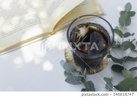A relaxing summer moment with iced coffee and a book; a refreshing table photo adorned with eucalyptus. A relaxing summer moment with iced coffee and a book; a refreshing table photo adorned with eucalyptus. 140858747