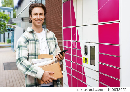 smiling man holding a parcel after a pickup from a delivery terminal. Ecommerce shopping and courier logistics make using this locker easy. smiling man holding a parcel after a pickup from a delivery terminal. Ecommerce shopping and courier logistics make using this locker easy. 140858951