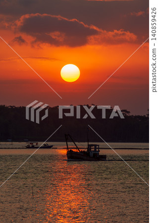 Beautiful golden sunset over the river with a small boat and sun reflection on the water. 140859426