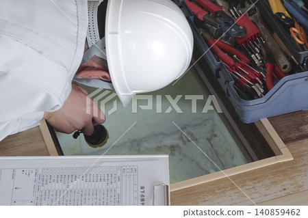 A worker inspects the area under the floor through an underfloor inspection hatch. A worker inspects the area under the floor through an underfloor inspection hatch. 140859462