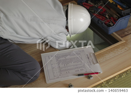 A worker inspects the area under the floor through an underfloor inspection hatch. 140859463