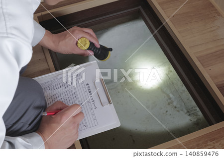 A worker inspects the area under the floor through an underfloor inspection hatch. A worker inspects the area under the floor through an underfloor inspection hatch. 140859476