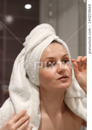 Woman touching up eye makeup in bathroom mirror 140859668