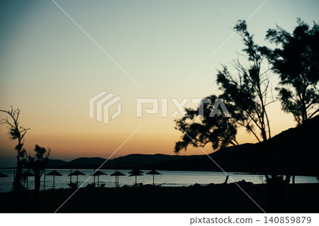 Tranquil Beach Sunset with Silhouetted Trees and Umbrellas 140859879