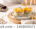 Two glasses of creamy chia seed pudding topped with vibrant diced mango and fresh coconut slices served on a ceramic plate with wooden spoons for a healthy breakfast or nutritious tropical snack 140860023