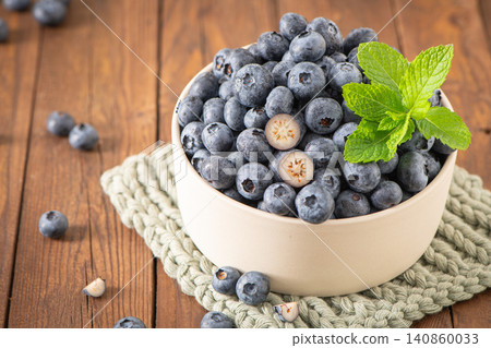 Fresh blueberries in a ceramic bowl with mint leaves on a wooden table, featuring vibrant fruit textures Fresh blueberries in a ceramic bowl with mint leaves on a wooden table, featuring vibrant fruit textures 140860033