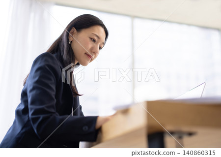 A young Japanese businesswoman operates a calculator by a bright window. A young Japanese businesswoman operates a calculator by a bright window. 140860315