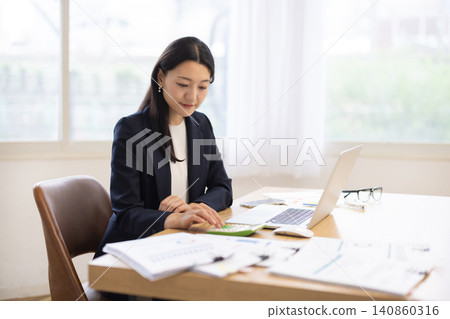 A young Japanese businesswoman operates a calculator by a bright window. A young Japanese businesswoman operates a calculator by a bright window. 140860316