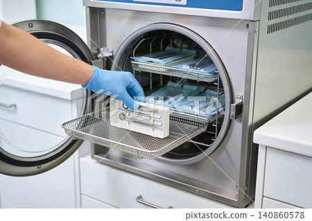 Dentist placing sterilized dental tools into an autoclave for disinfection Dentist placing sterilized dental tools into an autoclave for disinfection 140860578