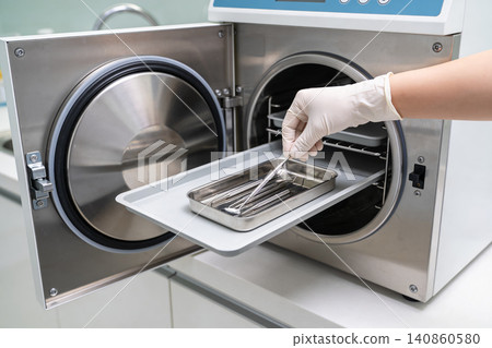 Dentist placing sterilized dental instruments into an autoclave for sterilization Dentist placing sterilized dental instruments into an autoclave for sterilization 140860580