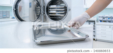 Gloved hand places sterile instrument tray into an open medical autoclave Gloved hand places sterile instrument tray into an open medical autoclave 140860653