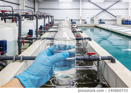 Water treatment facility with a hand holding a sample bottle for testing 140860733
