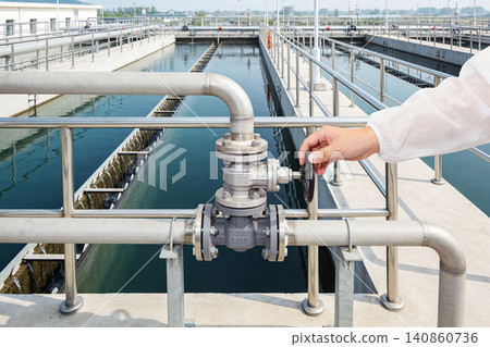 Worker operating valve at industrial water treatment plant with purification tanks Worker operating valve at industrial water treatment plant with purification tanks 140860736