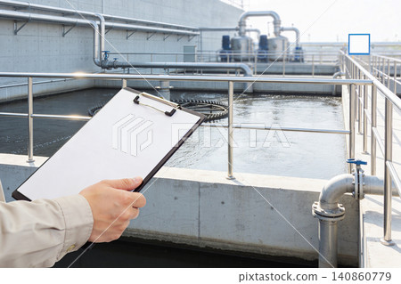Worker inspects water treatment plant with clipboard, checking industrial processes 140860779