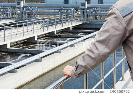 Worker overseeing industrial water treatment facility with aeration tanks and pipes Worker overseeing industrial water treatment facility with aeration tanks and pipes 140860792