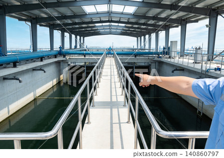 Water treatment plant with worker pointing at filtration system and blue pipes Water treatment plant with worker pointing at filtration system and blue pipes 140860797