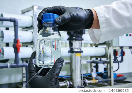 Scientist holding a clear liquid sample in a laboratory setting with filtration equipment Scientist holding a clear liquid sample in a laboratory setting with filtration equipment 140860985
