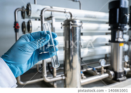 Scientist holding test tube with clear liquid near industrial water purification system Scientist holding test tube with clear liquid near industrial water purification system 140861001
