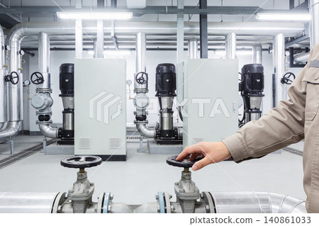 Industrial worker operating valve in a modern plant with complex piping and machinery Industrial worker operating valve in a modern plant with complex piping and machinery 140861033