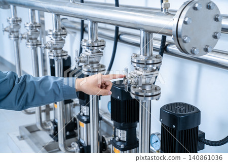 Industrial worker adjusts valve on complex stainless steel piping system with pumps 140861036