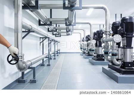 Industrial pump room with a technician adjusting a valve and rows of pumps Industrial pump room with a technician adjusting a valve and rows of pumps 140861064