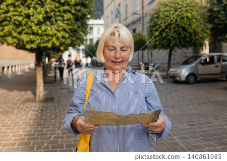 Happy senior female tourist holding paper map on beautiful European city street Happy senior female tourist holding paper map on beautiful European city street 140861085
