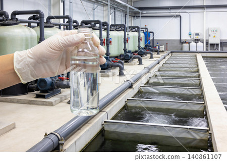 Water treatment plant technician holding sample in front of filtration tanks and basins Water treatment plant technician holding sample in front of filtration tanks and basins 140861107