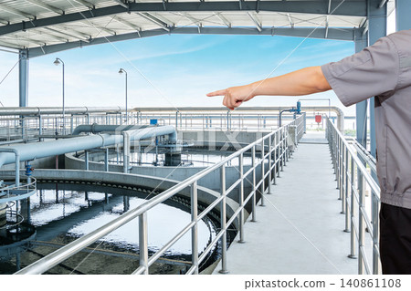 Worker points at industrial water treatment facility with large pipes and tanks 140861108