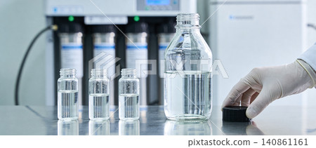 Scientist in sterile gloves handling laboratory glassware with clear liquid samples Scientist in sterile gloves handling laboratory glassware with clear liquid samples 140861161