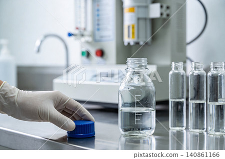 Scientist in gloves secures a blue cap on a glass laboratory bottle with liquid Scientist in gloves secures a blue cap on a glass laboratory bottle with liquid 140861166
