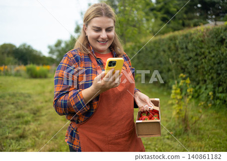 Happy young woman farmer holding strawberry box in garden 140861182