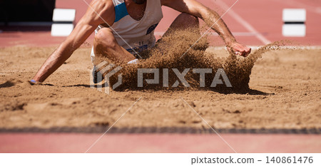 Male athlete long jump landing sand spray, landing in long jump in track and field Male athlete long jump landing sand spray, landing in long jump in track and field 140861476