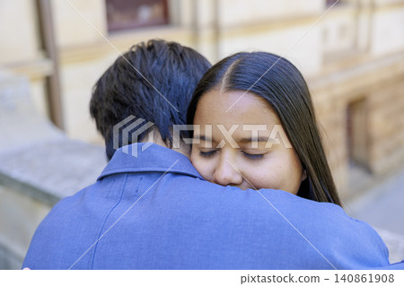 An international couple embracing; the woman's smile can be seen from behind. An international couple embracing; the woman's smile can be seen from behind. 140861908