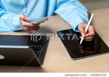 High view woman left hand use tablet pen write or take note on tablet while use right hand to work with mobile phone in home office. High view woman left hand use tablet pen write or take note on tablet while use right hand to work with mobile phone in home office. 140862030