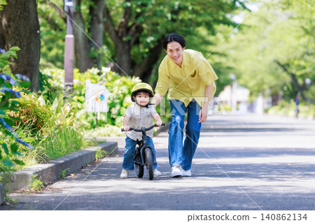 A boy practicing riding a bicycle with his dad. A boy practicing riding a bicycle with his dad. 140862134