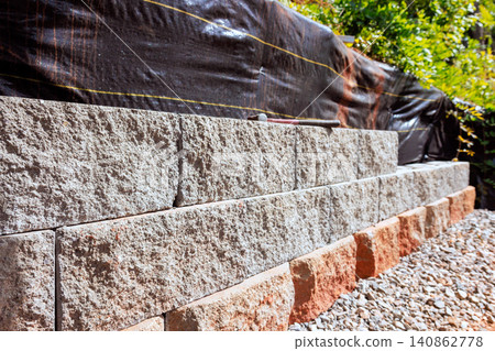 Workers are building stone retaining wall with gray orange blocks in garden setting Workers are building stone retaining wall with gray orange blocks in garden setting 140862778