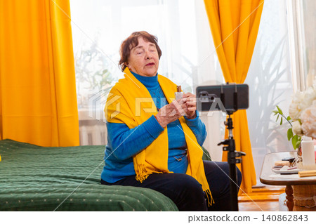 Elderly Caucasian woman talking about skincare routines during a live internet broadcast. Beauty blogging and social media concept. Active retirement and technology. Mid shot Elderly Caucasian woman talking about skincare routines during a live internet broadcast. Beauty blogging and social media concept. Active retirement and technology. Mid shot 140862843