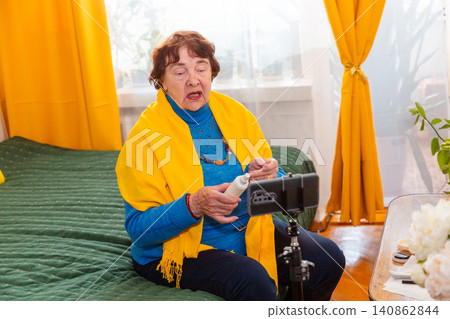 Elderly woman discussing cosmetic trends and personal care routines during an online session. Beauty blogging concept. Active senior participation in digital culture. Elderly woman discussing cosmetic trends and personal care routines during an online session. Beauty blogging concept. Active senior participation in digital culture. 140862844