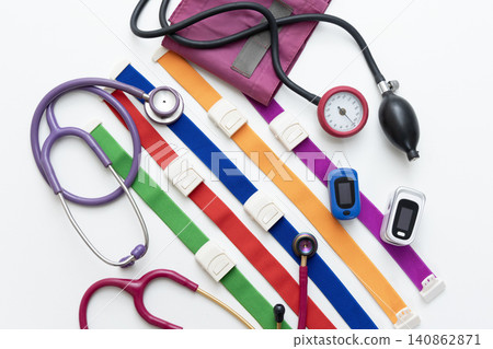 Colorful medical instruments lined up against a white background: a stethoscope, a blood pressure monitor, and a pulse oximeter. 140862871